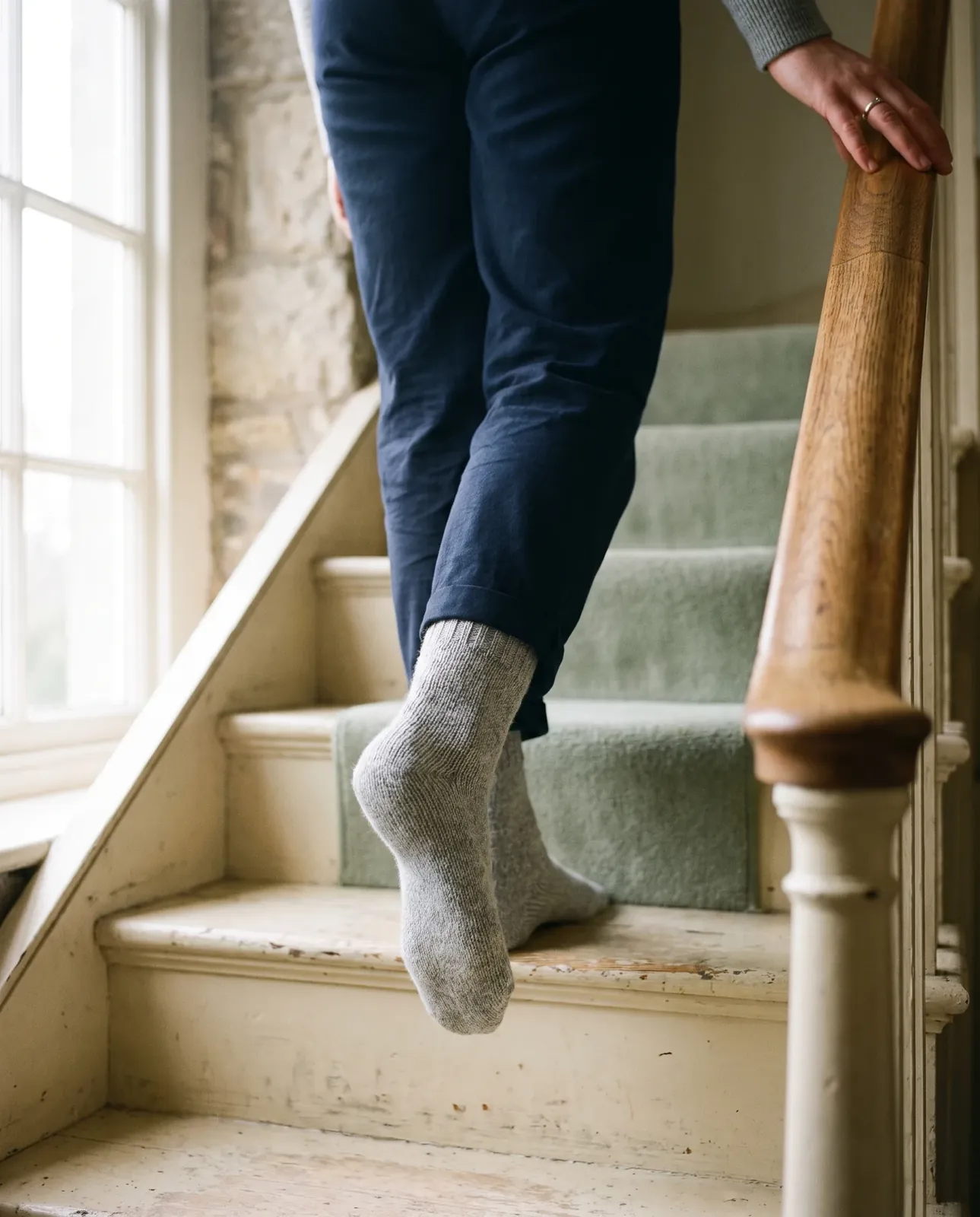 Feet in grey wool socks coming down a painted wooden staircase, a hand on the banister