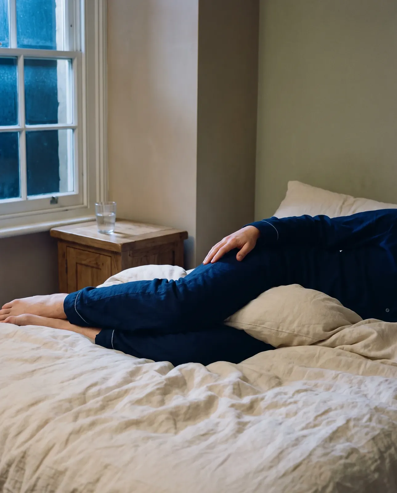 Lying on one side in bed with a pillow between the knees, a hand resting on the outer hip