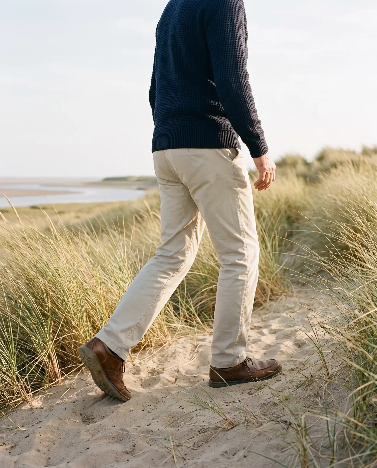 A man in a navy jumper walking easily along a sandy coastal path through the dunes