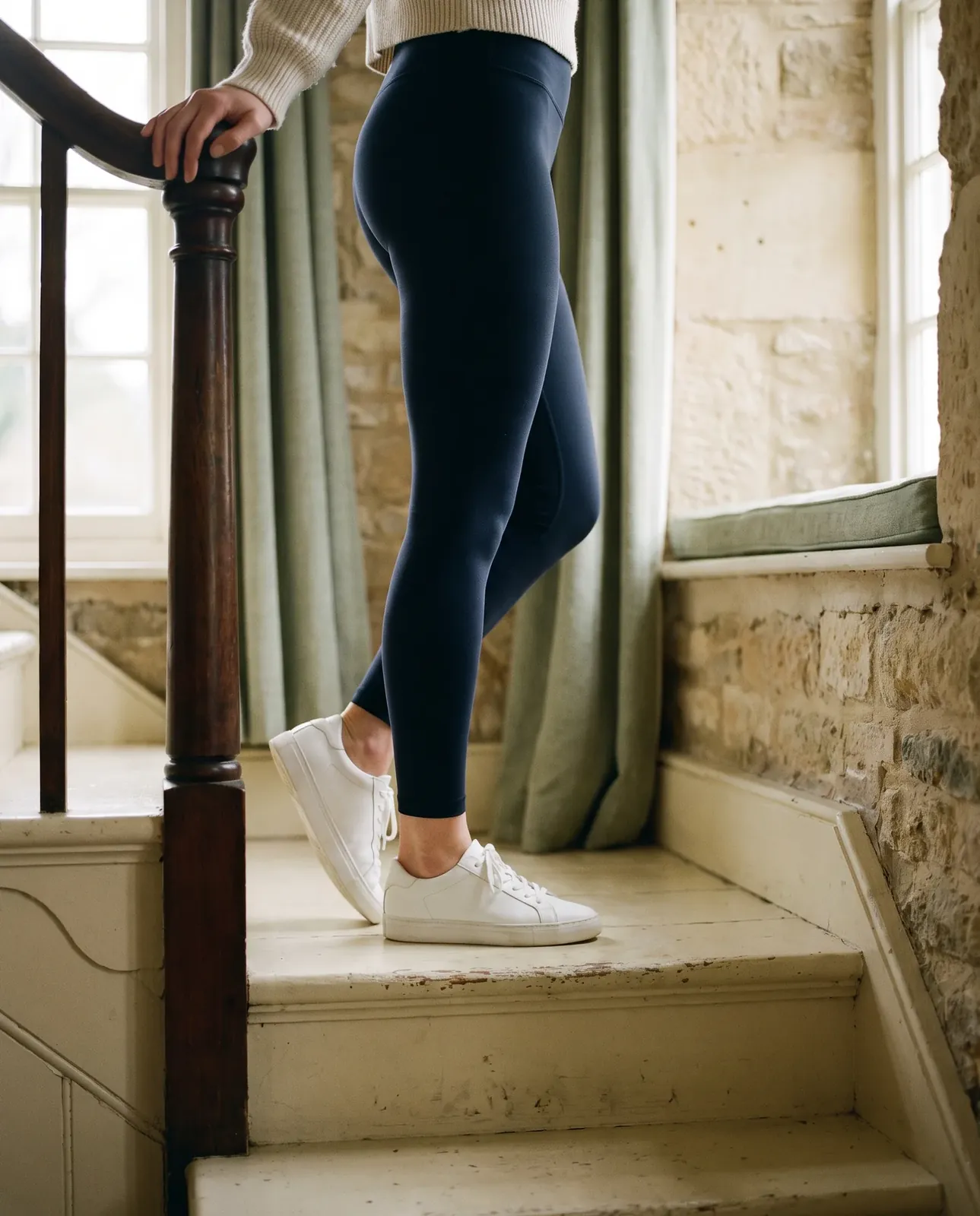 Legs in navy leggings and white trainers on a wooden staircase, rising onto the toes on the bottom step