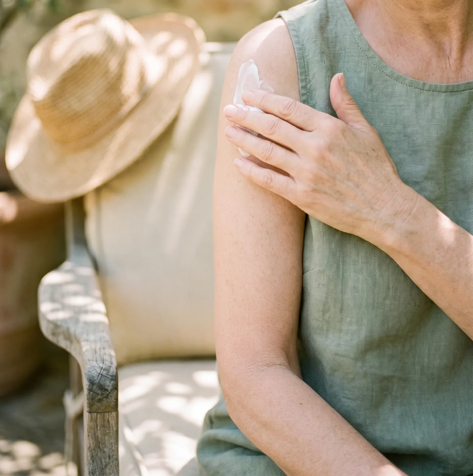 An older woman smoothing a little sun cream onto her shoulder in dappled garden light