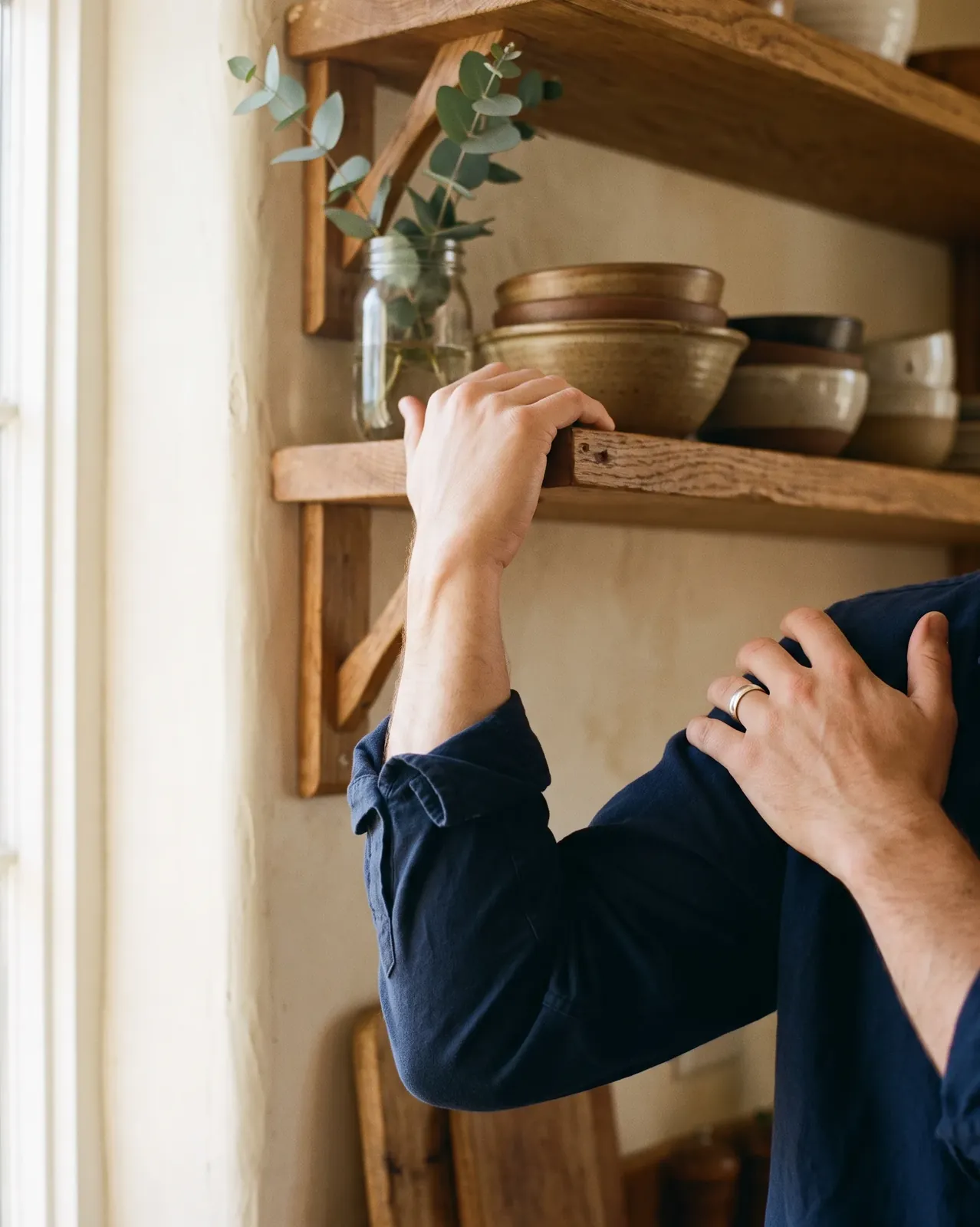 Person reaching up to a kitchen shelf while holding their sore shoulder
